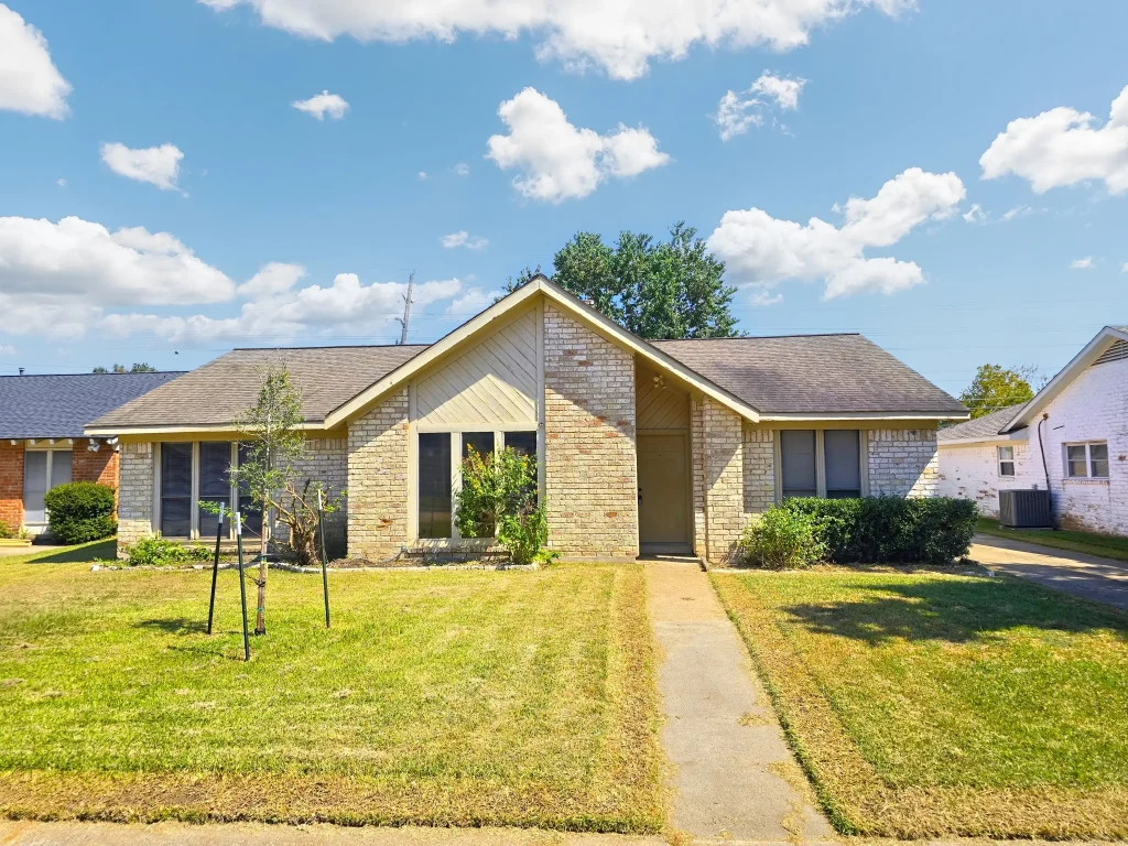 A single-story brick house with a centered front door, a neatly kept lawn, and a concrete walkway under a blue sky.